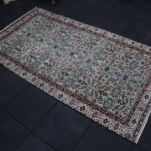 May include: A cream-colored rug with a floral pattern in shades of red, blue, and green. The rug has a border with a repeating design.