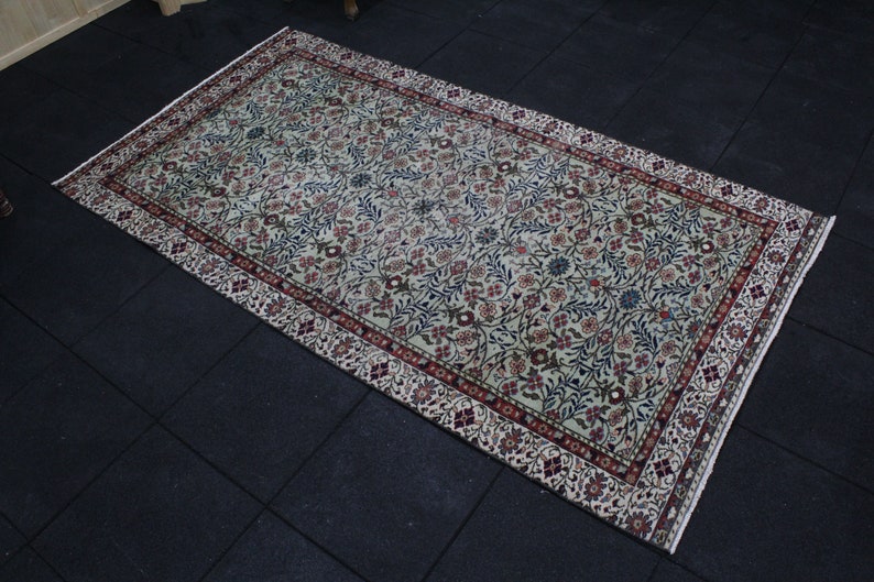 May include: A cream-colored rug with a floral pattern in shades of red, blue, and green. The rug has a border with a repeating design.