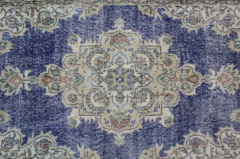 May include: A vintage rug with a blue background and a beige floral pattern. The rug has a worn and faded look, giving it a rustic and antique feel.