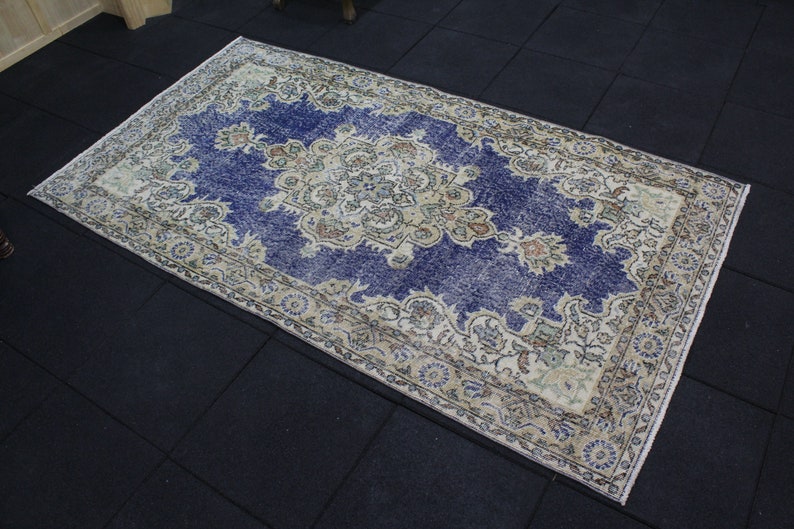 May include: A vintage rug with a blue background and a cream-colored floral pattern. The rug has a distressed look and is perfect for adding a touch of bohemian style to your home.