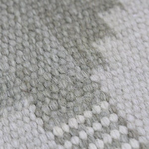 May include: Close-up of a white and gray woven rug with a textured surface.