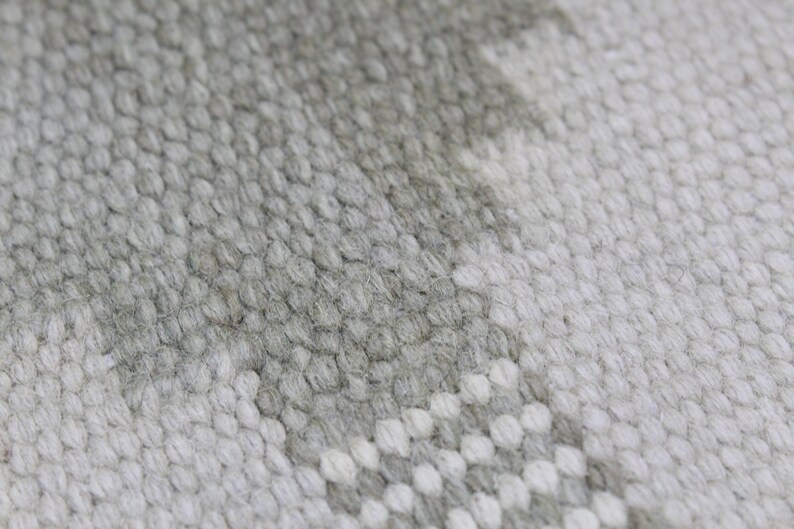 May include: Close-up of a white and gray woven rug with a textured surface.