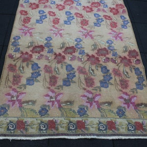 May include: A rectangular rug with a floral pattern in shades of red, blue, and pink on a beige background. The rug has a border with a repeating floral design. The rug is made of a woven material.