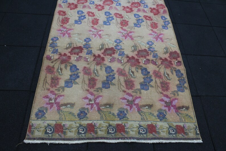 May include: A rectangular rug with a floral pattern in shades of red, blue, and pink on a beige background. The rug has a border with a repeating floral design. The rug is made of a woven material.