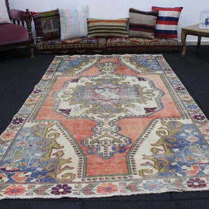 May include: A vintage Turkish rug with a cream background and a central medallion in shades of pink, blue, and green. The rug has a floral border in shades of pink, blue, and green.