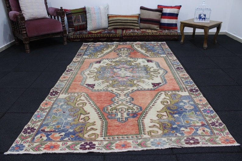 May include: A vintage Turkish rug with a cream background and a central medallion in shades of pink, blue, and green. The rug has a floral border in shades of pink, blue, and green.