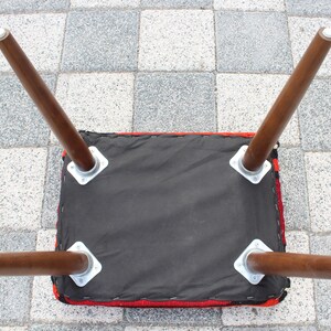 May include: The underside of a red and black upholstered stool with four wooden legs. The legs are attached to the stool with metal brackets.