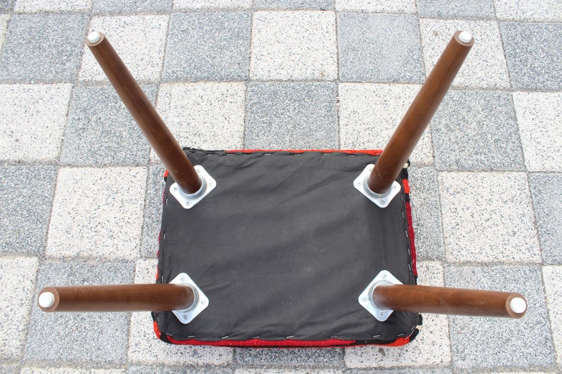 May include: The underside of a red and black upholstered stool with four wooden legs. The legs are attached to the stool with metal brackets.