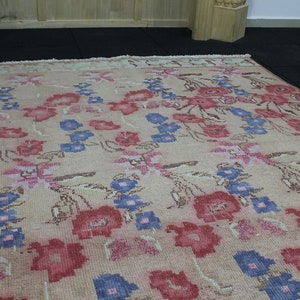May include: A rectangular rug with a floral pattern. The rug features a beige background with a repeating design of red, blue, and pink flowers. The flowers are stylized and arranged in rows across the rug's surface.