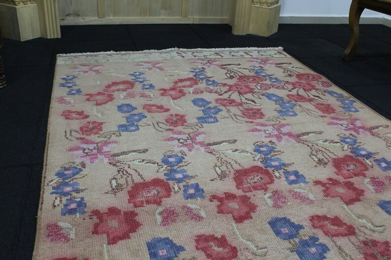 May include: A rectangular rug with a floral pattern. The rug features a beige background with a repeating design of red, blue, and pink flowers. The flowers are stylized and arranged in rows across the rug's surface.