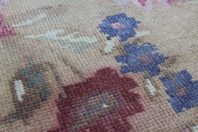 May include: Close-up of a beige rug with a floral pattern. The rug features flowers in shades of red, pink, and blue. The rug has a textured surface and a vintage aesthetic.