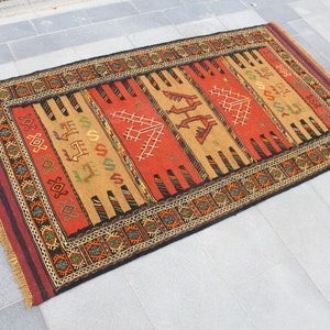 May include: A traditional Turkish rug with a red, orange, and brown color scheme. The rug features a geometric pattern with intricate details. The rug is made of wool and has a fringe border.