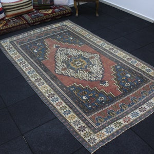 May include: A vintage rug with a red, blue, and white geometric pattern. The rug has a faded, distressed look and is made of wool.