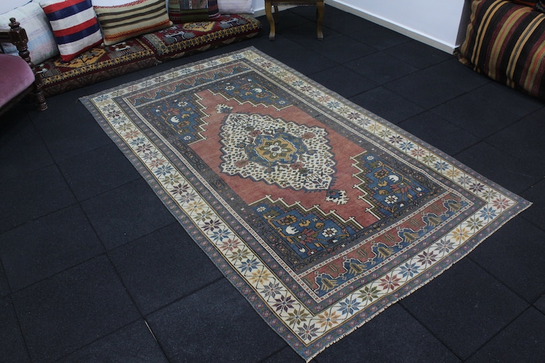 May include: A vintage rug with a red, blue, and white geometric pattern. The rug has a faded, distressed look and is made of wool.