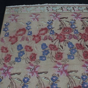 May include: Beige floral rug with a repeating pattern of red, blue, and pink flowers. The rug has a faded, vintage look with a fringed edge. The flowers are stylized and arranged in rows.