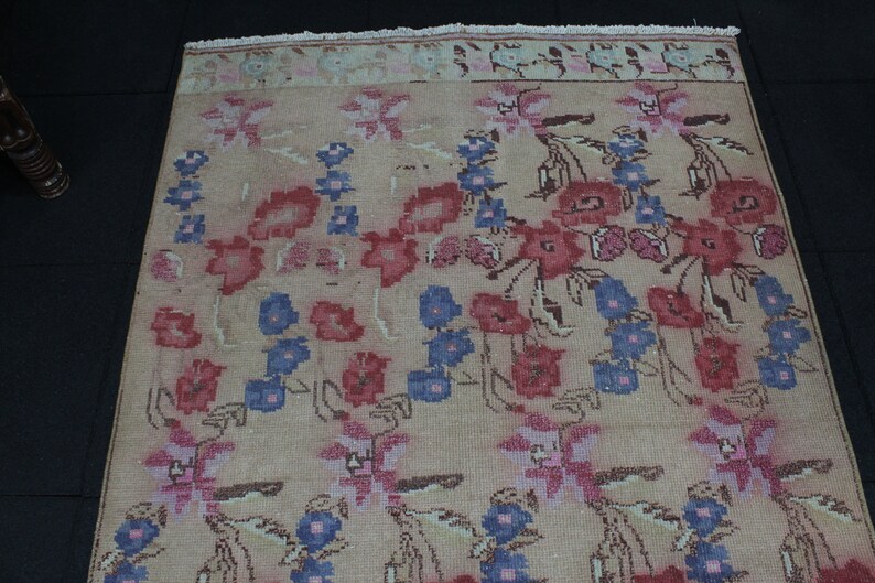 May include: Beige floral rug with a repeating pattern of red, blue, and pink flowers. The rug has a faded, vintage look with a fringed edge. The flowers are stylized and arranged in rows.