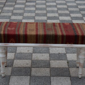 May include: A white wooden bench with distressed paint and a colourful striped woven cushion.