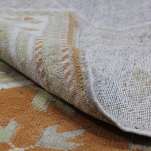 May include: Close-up of a beige and orange patterned rug with a fringe edge. The rug is folded over, revealing the beige backing.