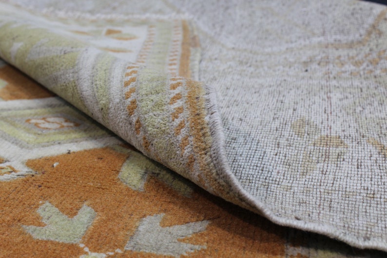 May include: Close-up of a beige and orange patterned rug with a fringe edge. The rug is folded over, revealing the beige backing.