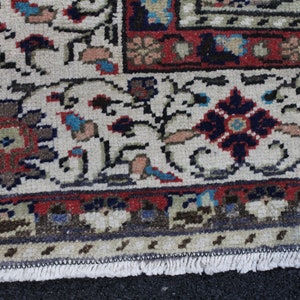May include: Close-up of the fringe edge of a cream-colored rug with a floral pattern in shades of red, blue, and brown. The rug has a traditional Persian design.