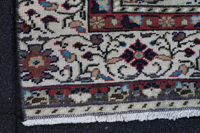 May include: Close-up of the fringe edge of a cream-colored rug with a floral pattern in shades of red, blue, and brown. The rug has a traditional Persian design.