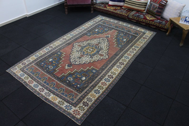 May include: A vintage Turkish rug with a red, blue, and cream color scheme. The rug has a central medallion with intricate floral designs and a border with repeating star motifs.