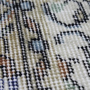 May include: Close-up of a beige, blue, and brown patterned rug with a textured surface. The rug has a woven design with small, raised loops.
