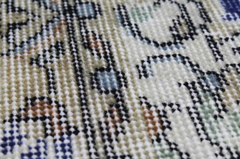 May include: Close-up of a beige, blue, and brown patterned rug with a textured surface. The rug has a woven design with small, raised loops.