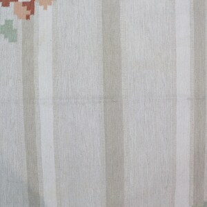 Puede incluir: Primer plano de una alfombra de rayas blancas y beige con una textura sutil tejida. La alfombra tiene un patr&oacute;n floral en tonos azules, rosas y naranjas.
