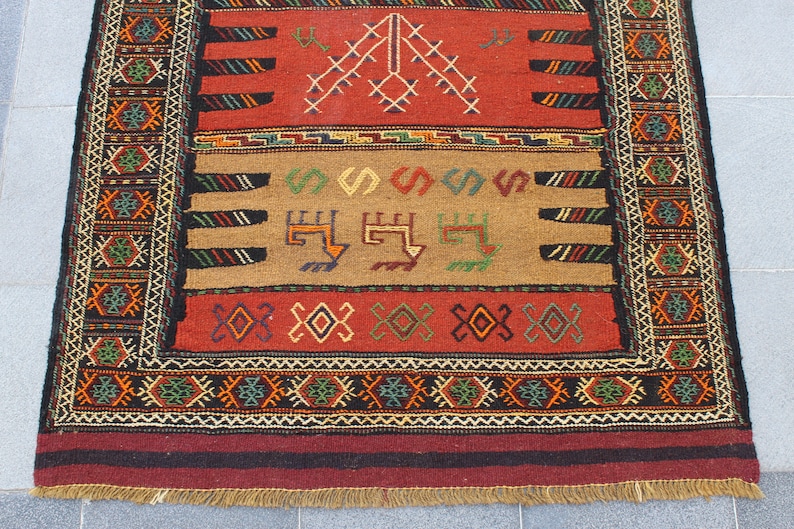 May include: A traditional rug with a red, brown, and black color scheme. The rug features intricate geometric patterns and a fringe border.