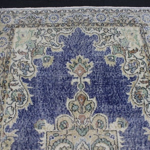May include: A vintage rug with a blue center and a cream-colored border. The rug has a floral pattern with intricate details.