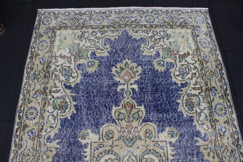 May include: A vintage rug with a blue center and a cream-colored border. The rug has a floral pattern with intricate details.