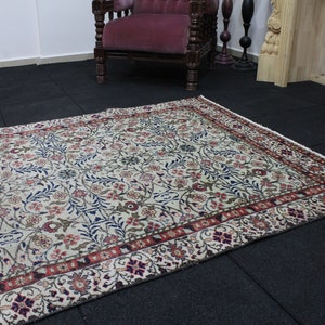 May include: A cream-colored rug with a floral pattern in shades of red, blue, and green. The rug has a border with a repeating pattern of red, white, and blue.