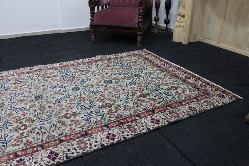 May include: A cream-colored rug with a floral pattern in shades of red, blue, and green. The rug has a border with a repeating pattern of red, white, and blue.