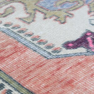 May include: Close-up of a woven rug with a pink, purple, and blue butterfly design on a cream background. The rug has a red and white border.
