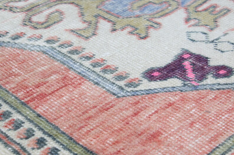 May include: Close-up of a woven rug with a pink, purple, and blue butterfly design on a cream background. The rug has a red and white border.