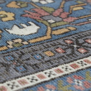 May include: Close-up of a blue, gray, and white patterned rug with a detailed woven design. The rug has a fringe border.