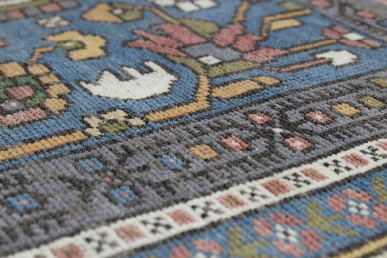 May include: Close-up of a blue, gray, and white patterned rug with a detailed woven design. The rug has a fringe border.