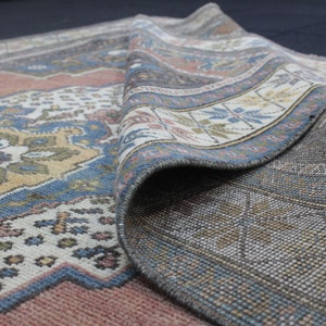 May include: A vintage rug with a colorful geometric pattern in shades of blue, red, and beige. The rug is folded in half, revealing the intricate details of the woven design.