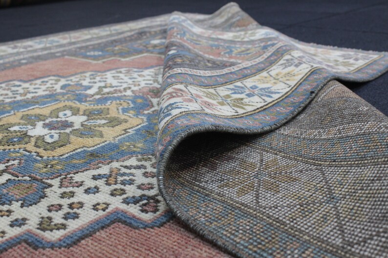 May include: A vintage rug with a colorful geometric pattern in shades of blue, red, and beige. The rug is folded in half, revealing the intricate details of the woven design.