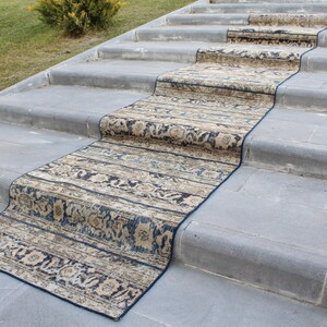 May include: A patterned runner rug in shades of beige, brown, and blue is laid out on a set of concrete steps. The rug has a traditional design with floral motifs.