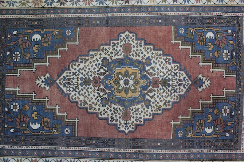 May include: A vintage rug with a red background and a central medallion featuring a blue, yellow, and green floral design. The rug has a border with a repeating pattern of blue, white, and red.