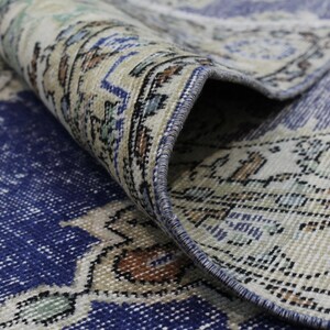 May include: Close-up of a blue and cream patterned rug with a fringed edge. The rug is folded over, showing the underside of the fabric.