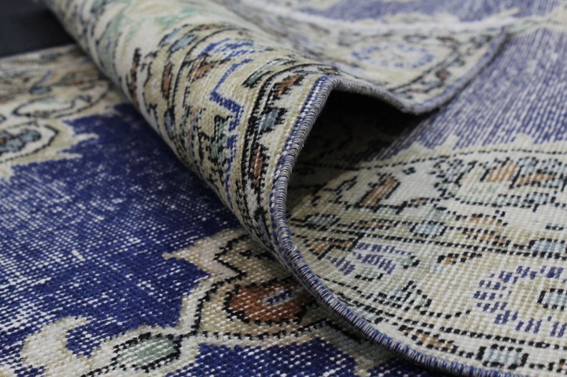 May include: Close-up of a blue and cream patterned rug with a fringed edge. The rug is folded over, showing the underside of the fabric.