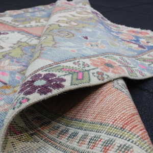 May include: A vintage rug with a blue, pink, and green floral pattern. The rug is folded in half, showing the intricate details of the design.