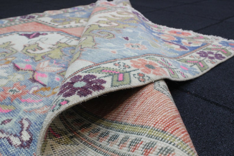 May include: A vintage rug with a blue, pink, and green floral pattern. The rug is folded in half, showing the intricate details of the design.