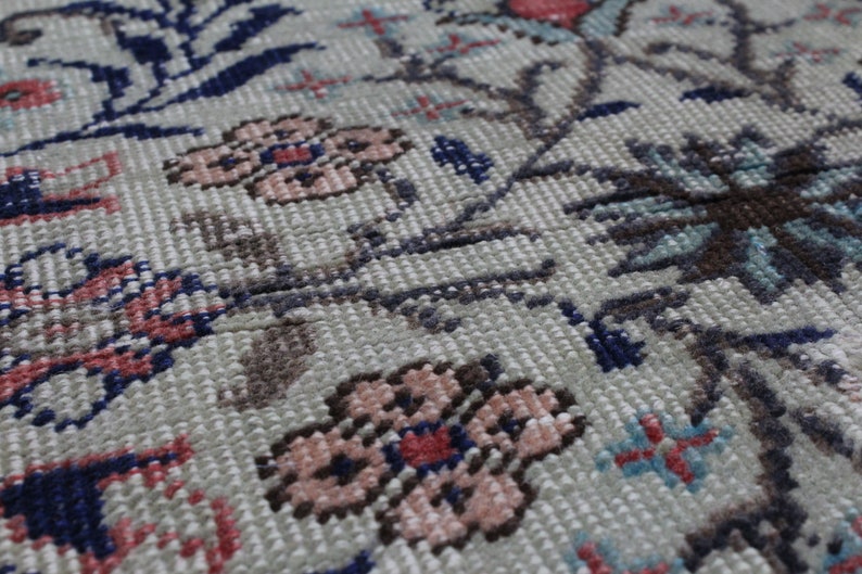 May include: Close-up of a beige rug with a floral pattern. The rug features pink, red, blue, and brown flowers on a beige background.