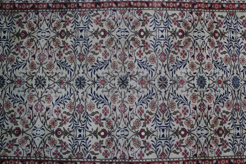 May include: A vintage rug with a cream background and a floral pattern in shades of blue, red, and brown. The rug has a border with a repeating pattern.