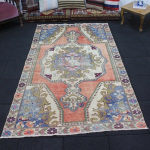 May include: A vintage rug with a floral pattern in shades of pink, blue, and beige. The rug has a central medallion with a geometric design and a border with a repeating floral motif.
