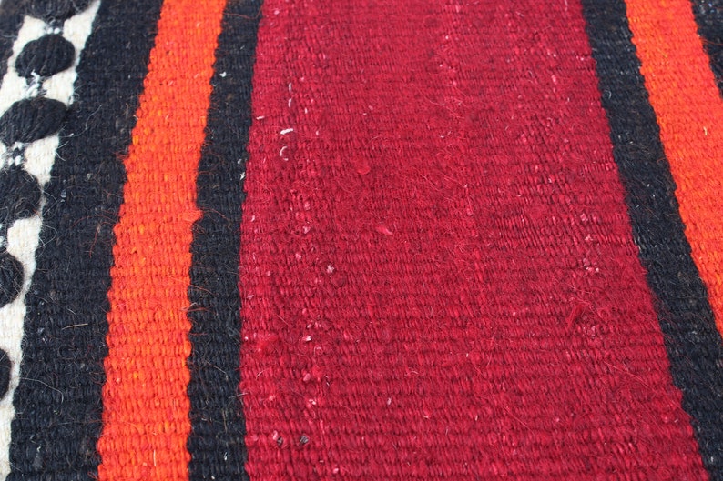 May include: Close-up of a woven fabric with stripes of red, orange, black, and white.